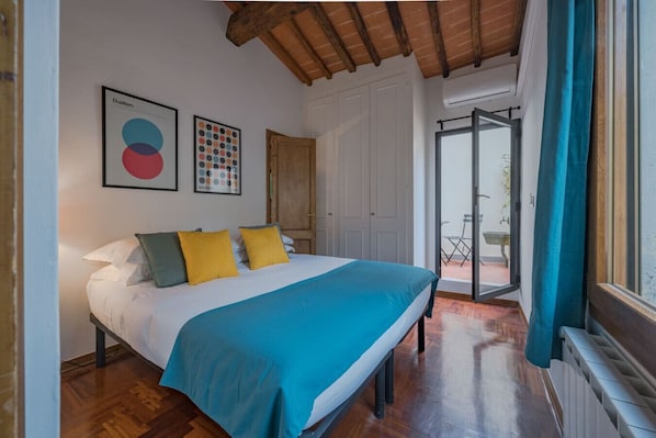 A bedroom with a bed, a wooden ceiling, a door, and a view through a window.