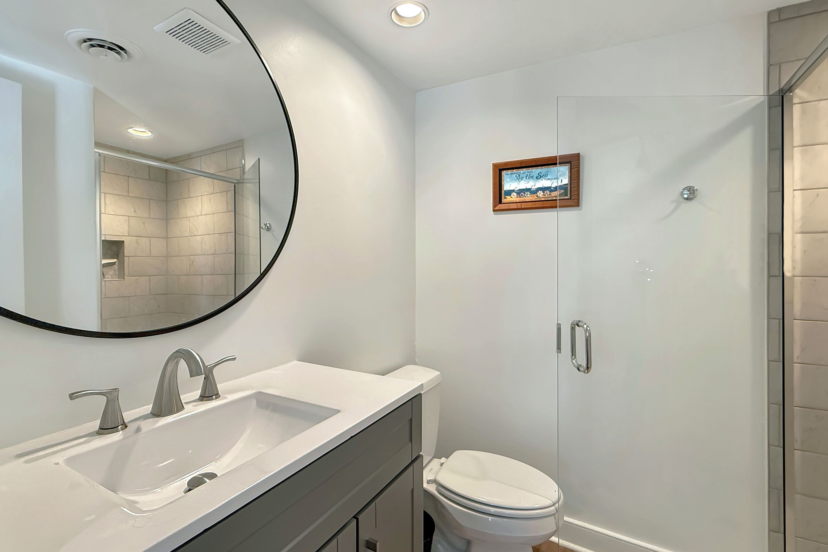 A modern bathroom with a white sink, two faucets, a mirror, and a framed picture on the wall.