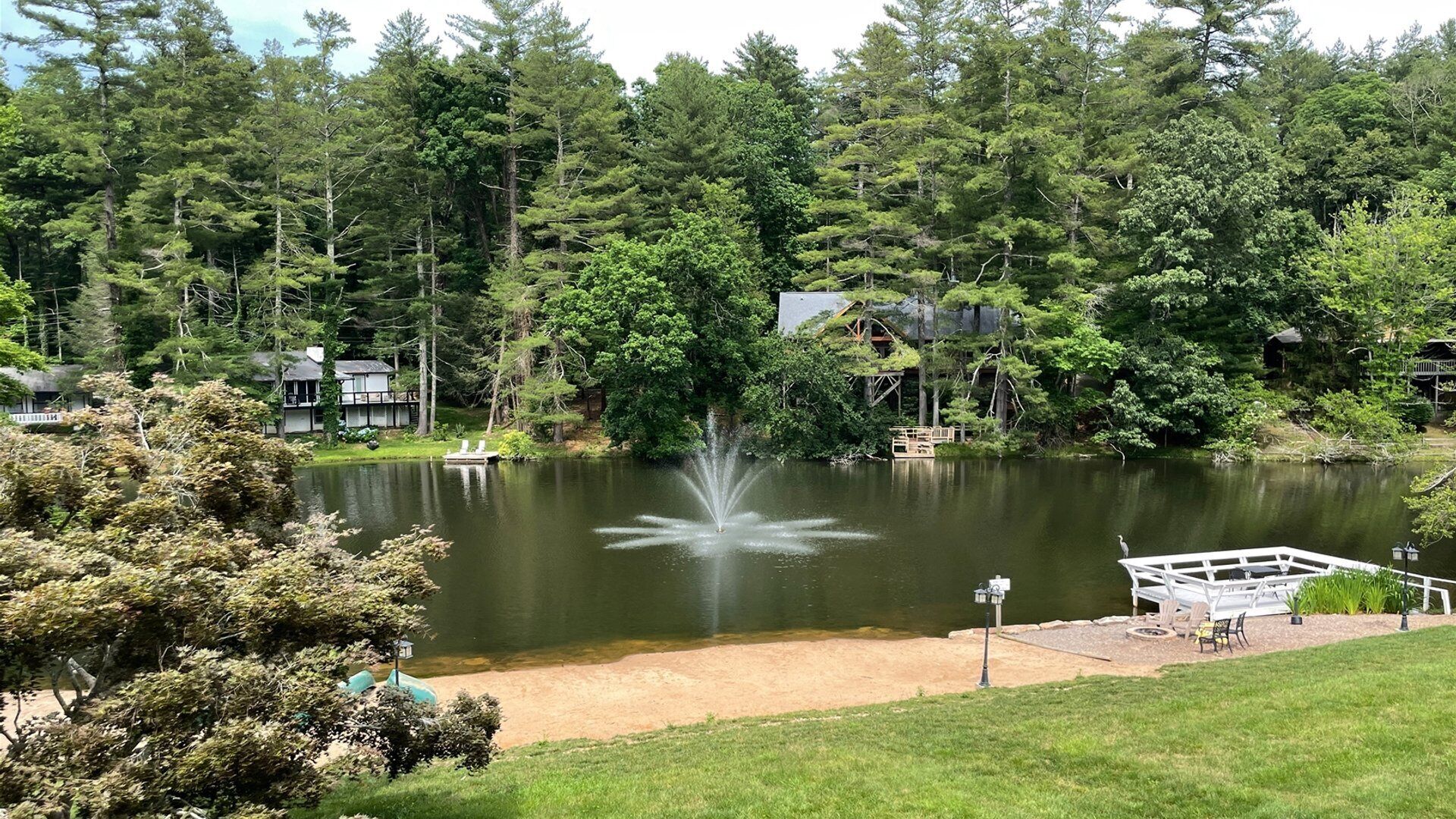 Um lago com uma fonte, cercado por árvores densas e casas.