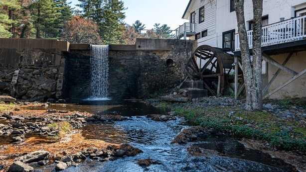 Un puente de piedra rústico con una cascada, un arroyo pequeño y una rueda hidráulica de madera.