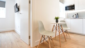 A modern kitchen with white cabinets, a microwave, and a sink. There is a dining area with a table and two chairs, and a small potted plant on the table. -  StayPrime Marylebone Serviced Apartments (London)