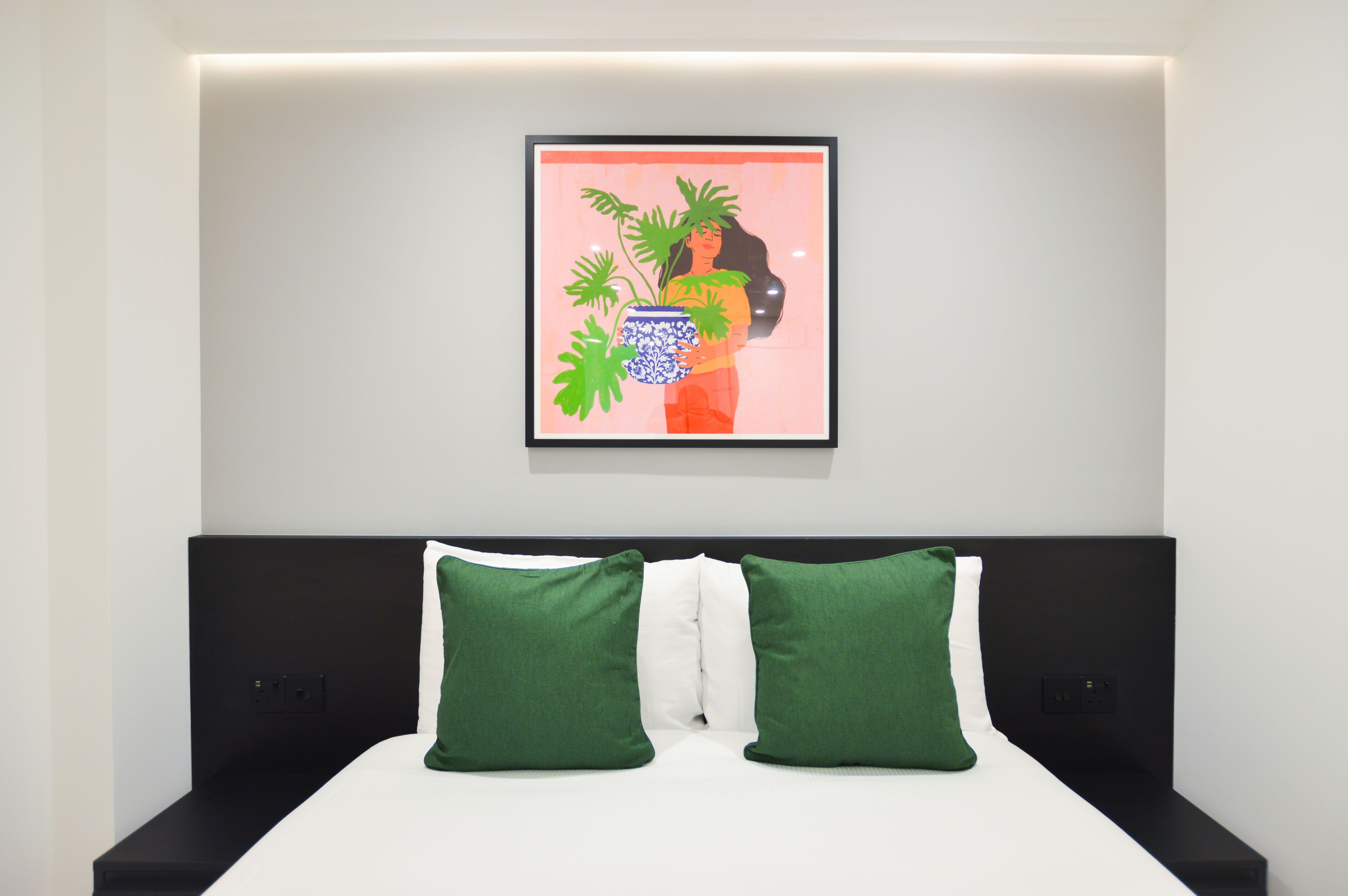 Ein modernes Schlafzimmer mit einem Bett, grünen und weißen Kissen und einem gerahmten Kunstwerk an der Wand.