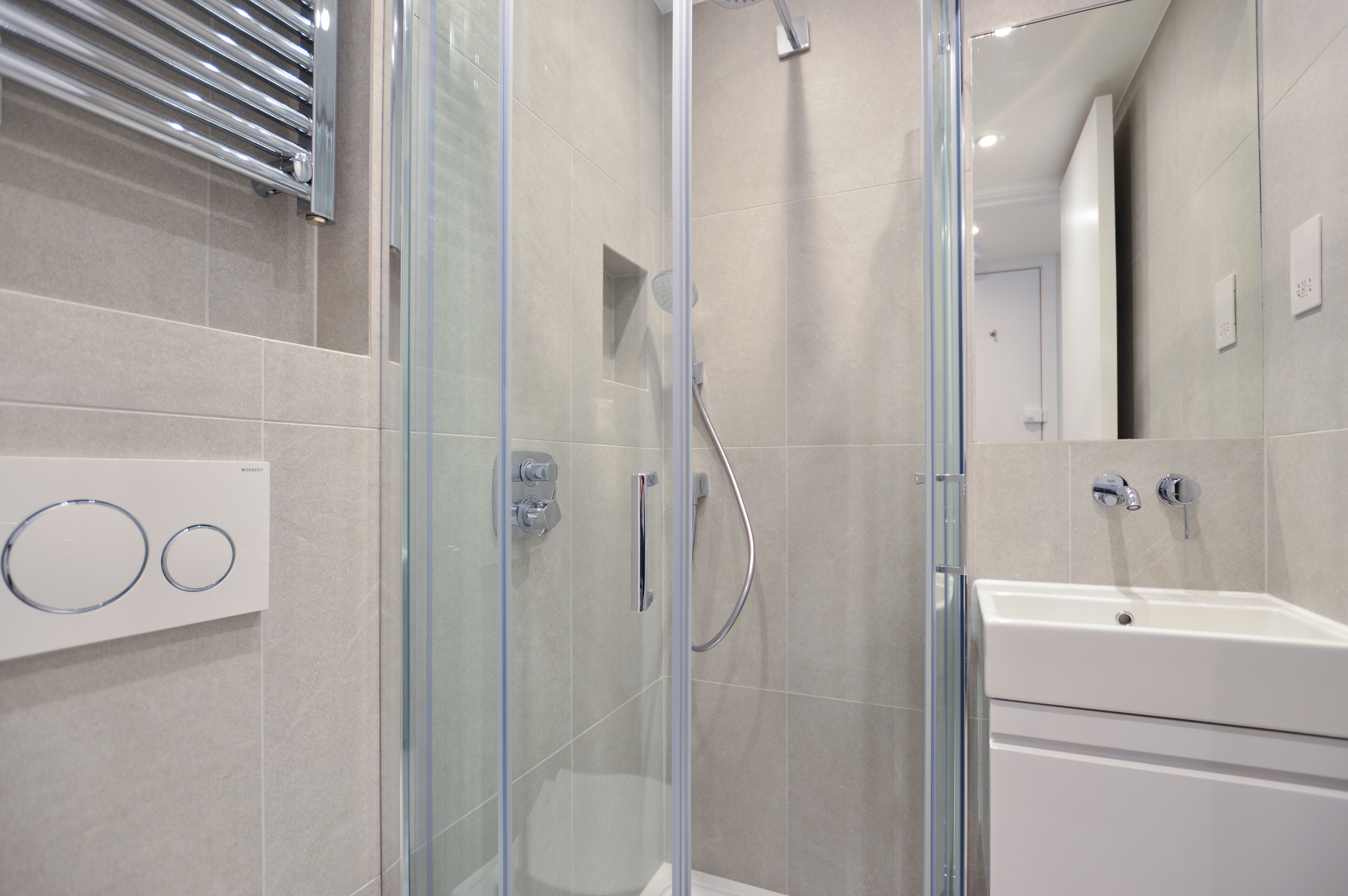 Un baño moderno con ducha de vidrio, lavamanos blanco y toallero.