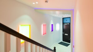 A modern hotel hallway with a staircase, illuminated by colorful wall lights and a ceiling light fixture. -  StayPrime Marylebone Serviced Apartments (London)
