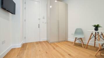 A modern room with a wooden floor, a white door, a wardrobe, a small table with a plant, and a chair.