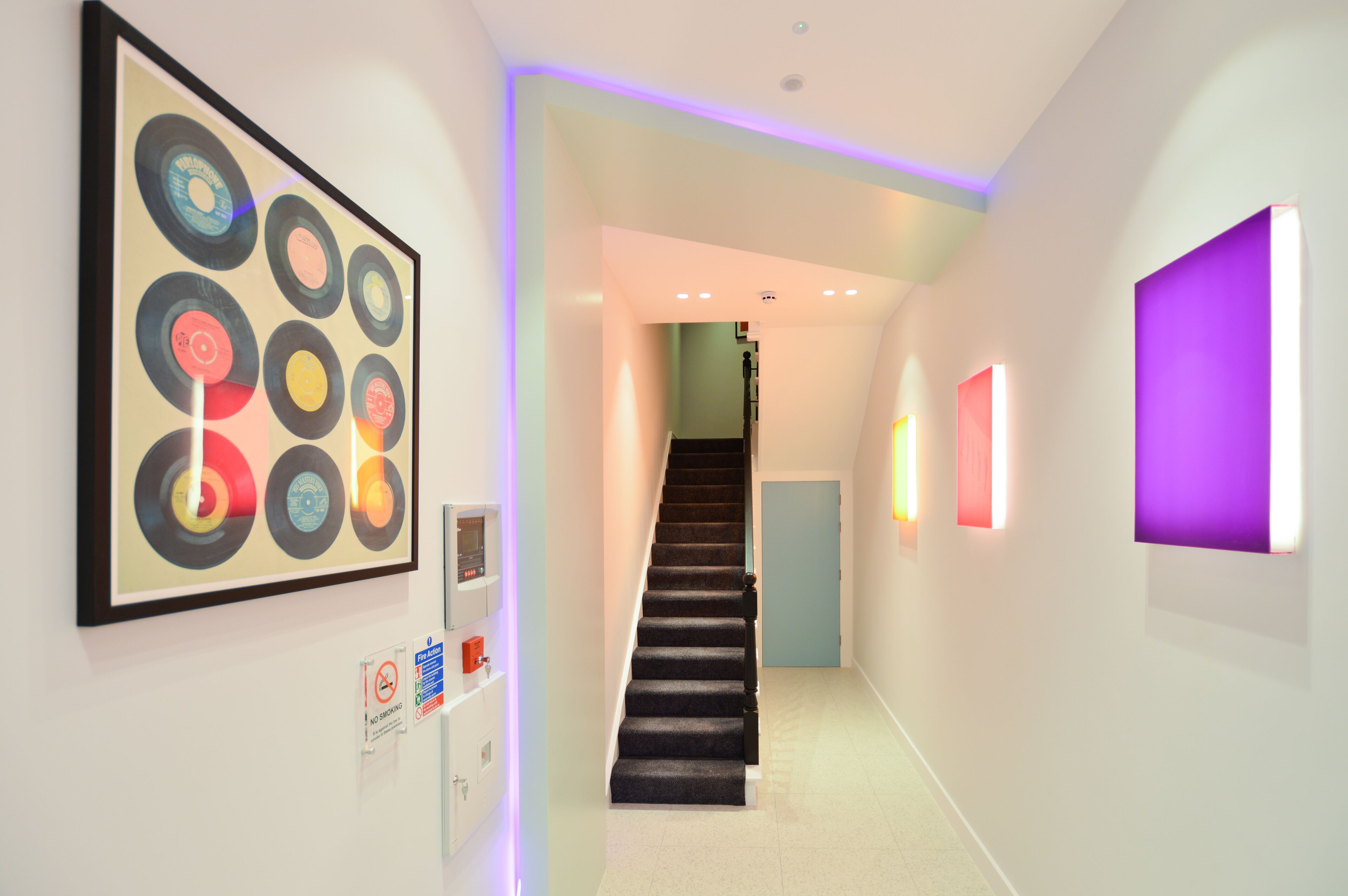 Un couloir moderne avec un escalier, des œuvres d’art encadrées et des luminaires fixés au mur.