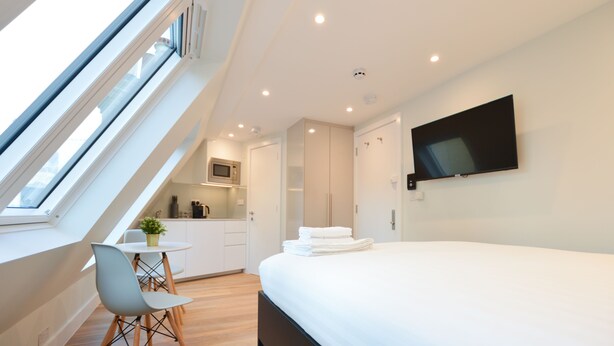 A modern hotel room with a skylight, a bed, a TV, and a kitchenette. -  StayPrime Marylebone Serviced Apartments (London)