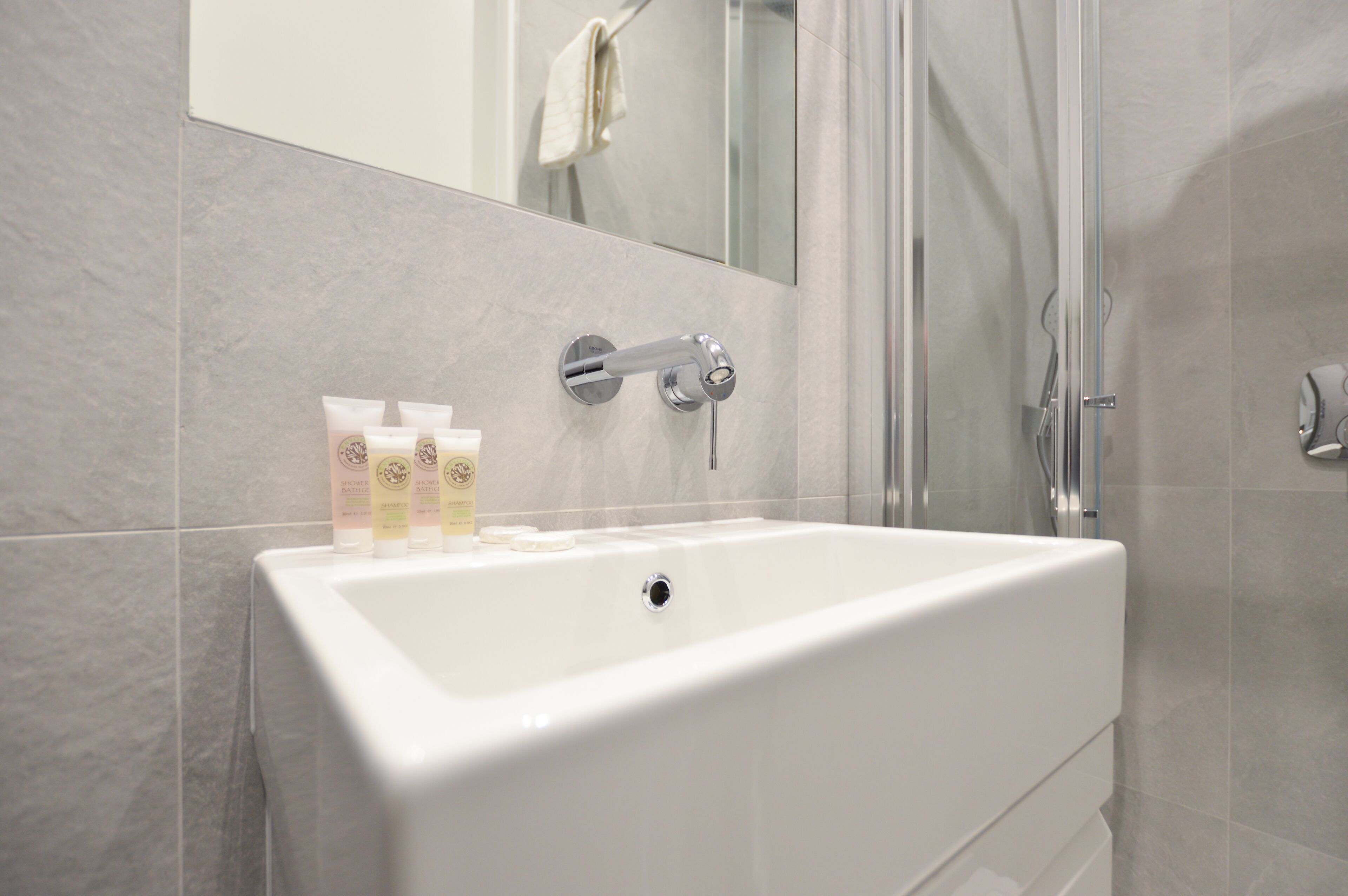 Une salle de bain moderne avec un lavabo blanc, une douche en verre et des articles de toilette posés sur le lavabo.