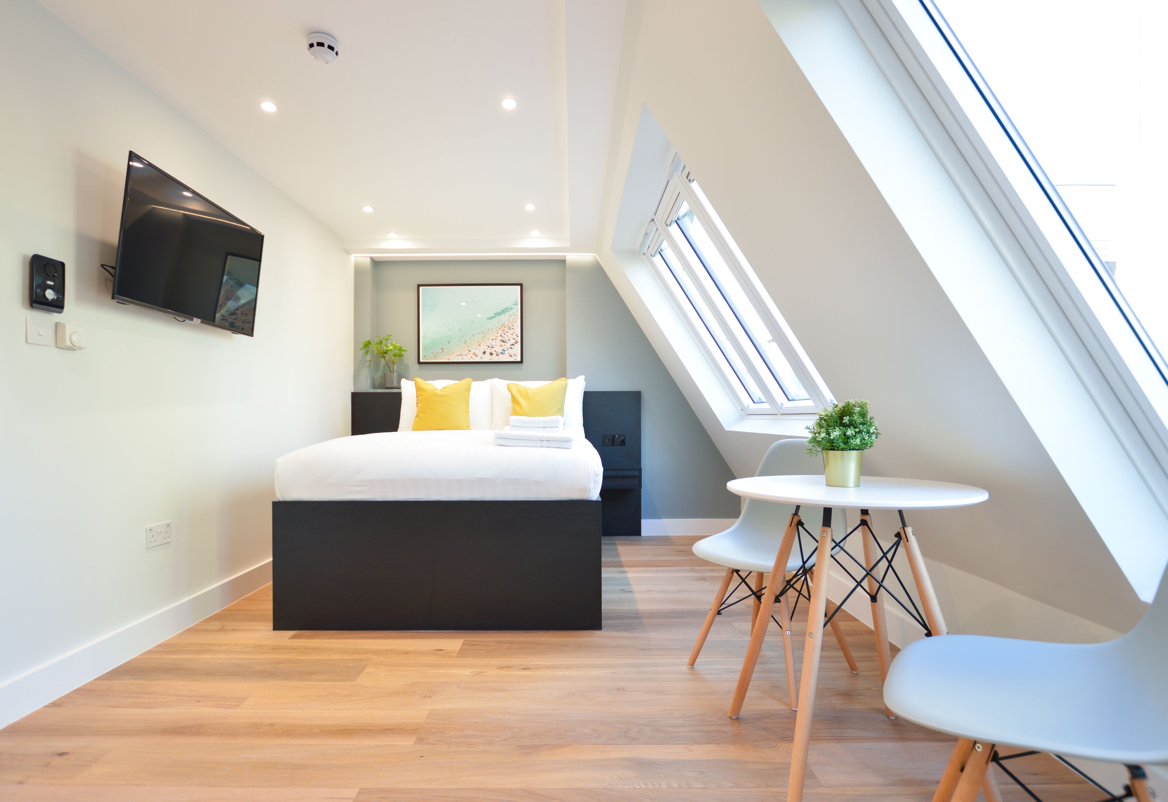 Ein modernes Schlafzimmer mit Bett, Fernseher, einem kleinen Tisch mit Stühlen und einem Oberlicht.