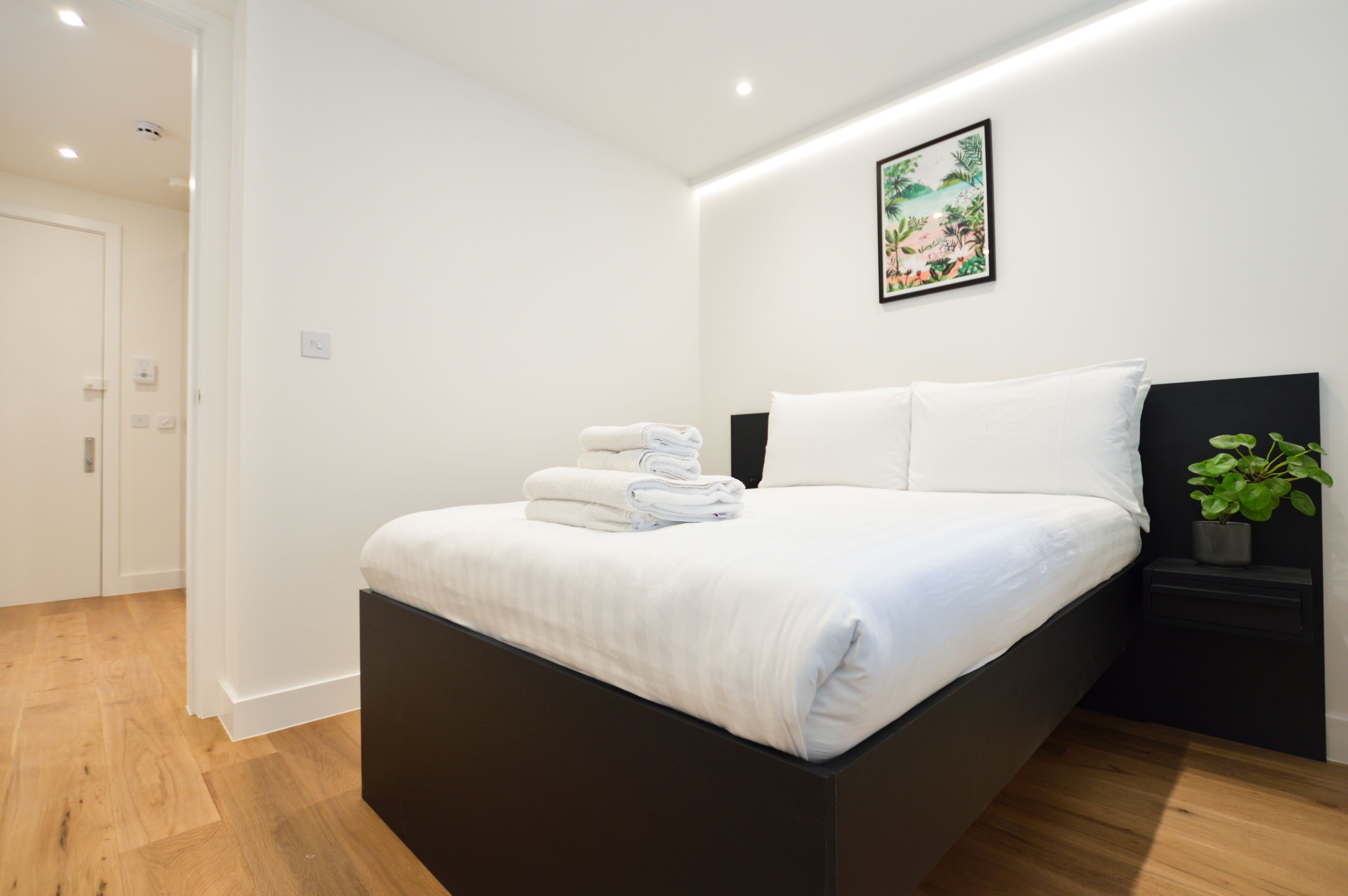 Un dormitorio moderno con una cama grande, una mesita de noche con una planta y un cuadro en la pared.