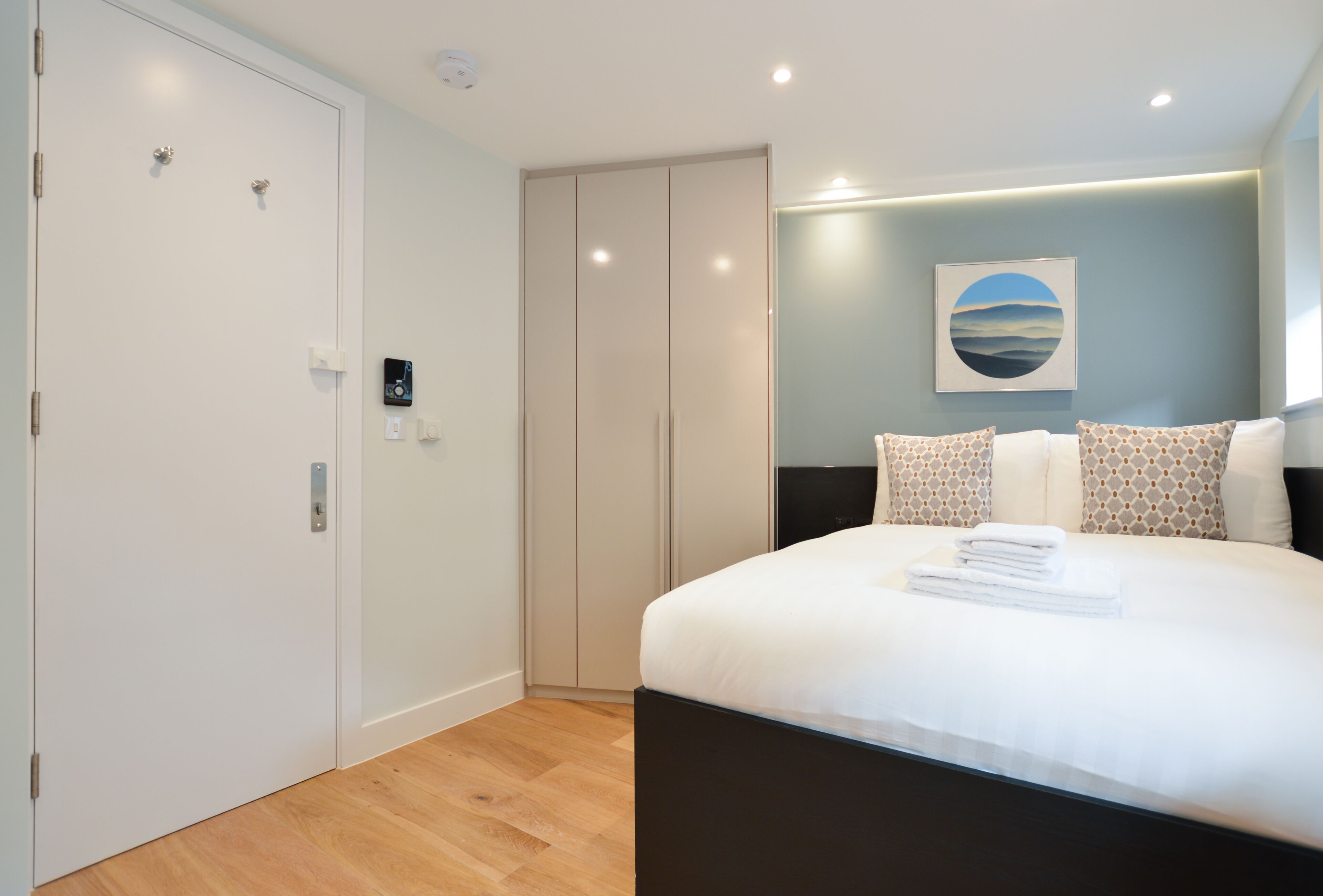 A modern bedroom with a large bed, a wardrobe, and a wall-mounted artwork.