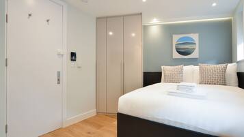 A modern bedroom with a large bed, a wardrobe, and a wall-mounted artwork.