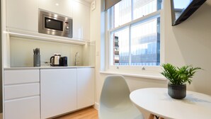 A modern kitchen with white cabinets, a stainless steel microwave, a coffee maker, and a potted plant on a small table. -  StayPrime Marylebone Serviced Apartments (London)
