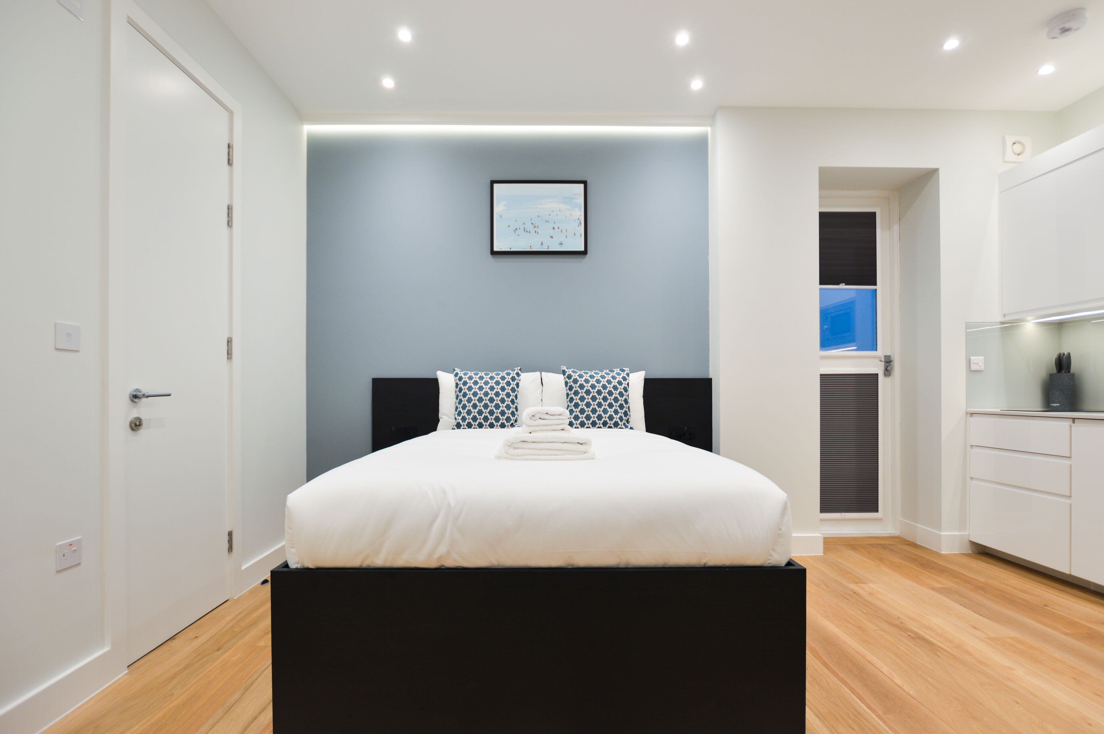 A modern bedroom with a bed, a bedside table, a wall-mounted picture, and a window.