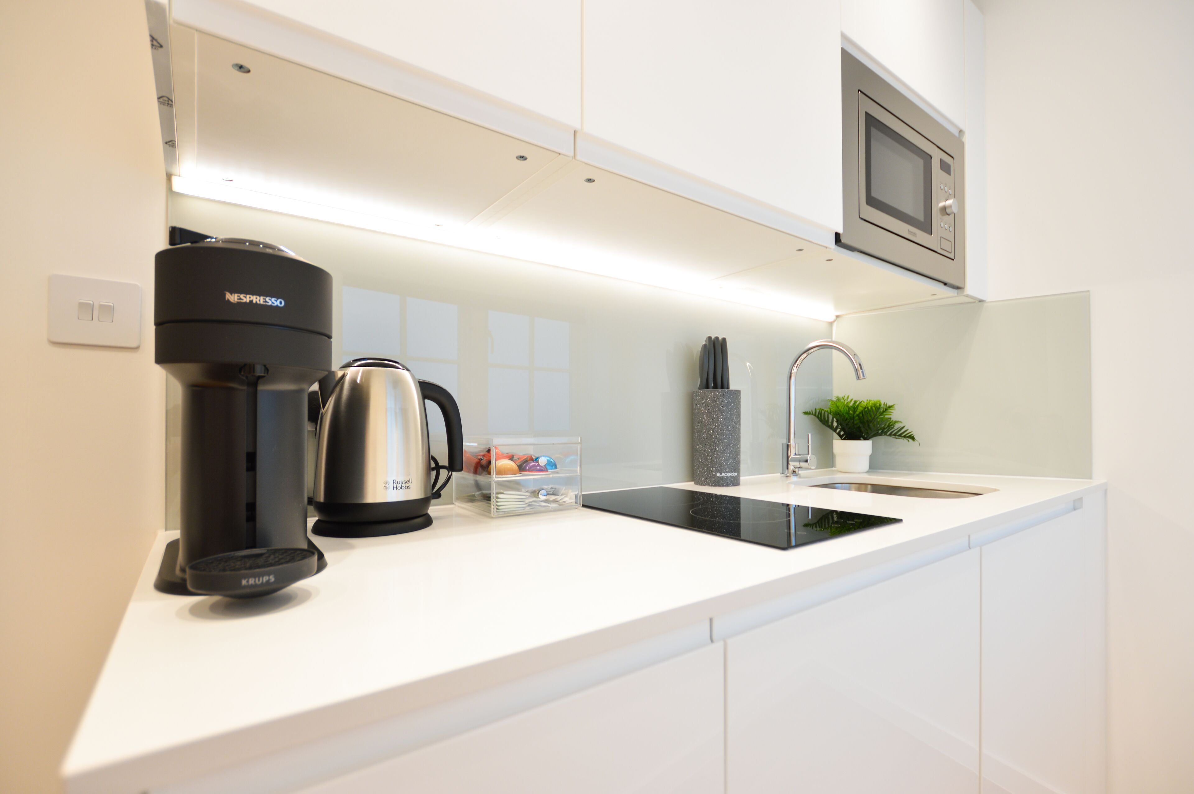 A modern kitchen with a coffee maker, kettle, and a sink.