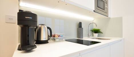 A modern kitchen with a coffee maker, kettle, and a sink.