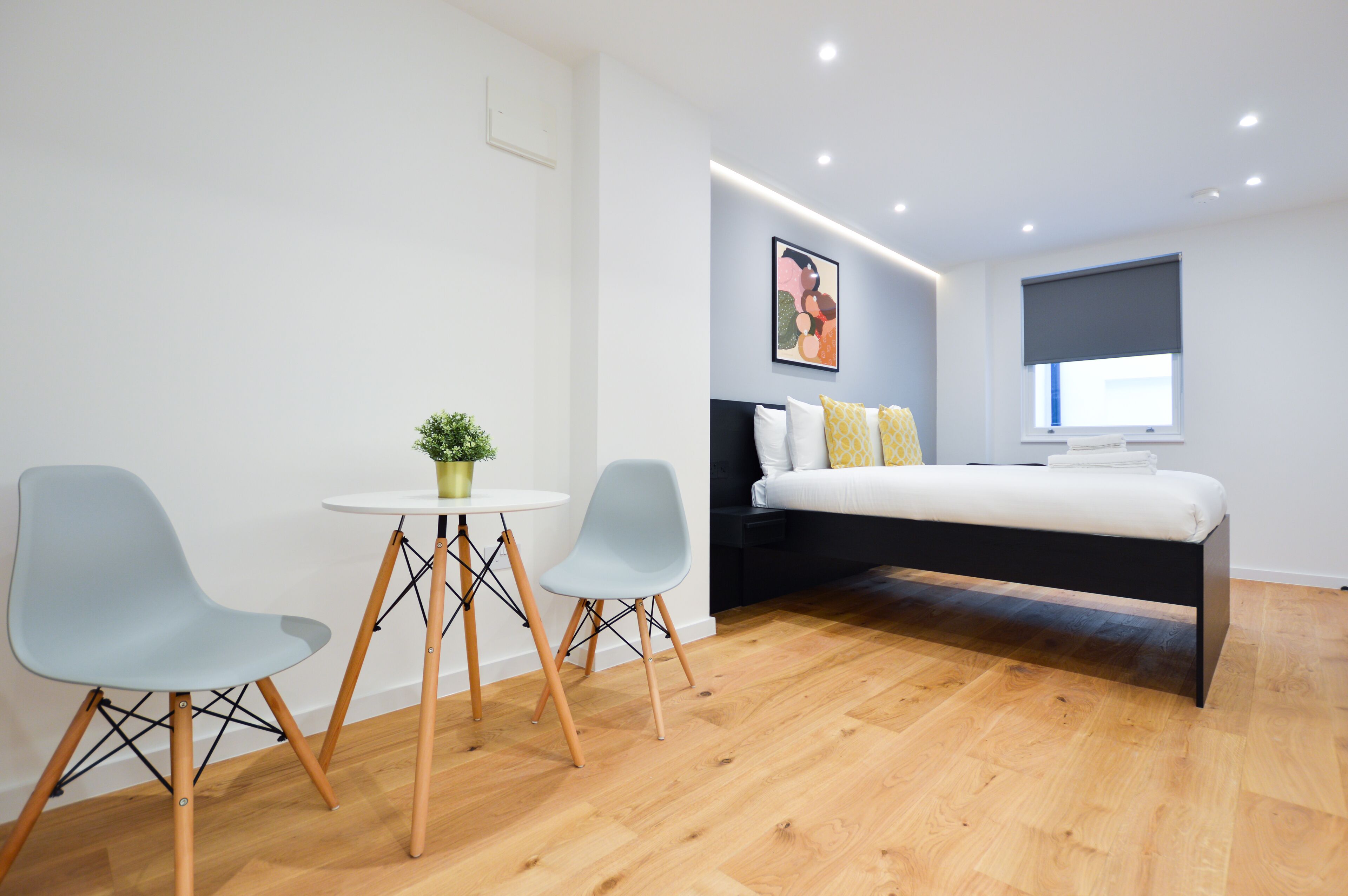 A modern bedroom with a bed, two chairs, a small table, and a potted plant.