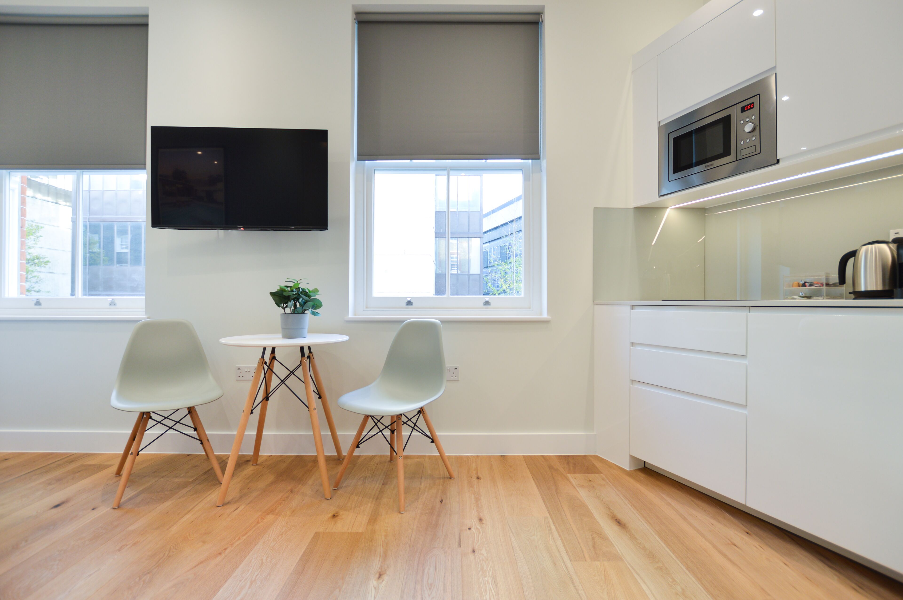 A modern kitchen with a built-in microwave, a flat-screen TV, and a dining area with two chairs and a small table.