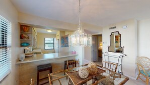 A modern kitchen with a dining area, featuring a chandelier, wooden furniture, and a large mirror. - Prime Location I Free Beach Access Directly Across The Street!!! (Marco Island)