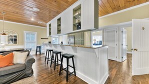 Una cocina moderna con armarios blancos, una isla central con taburetes y techo de madera.