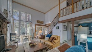 Un vaste salon doté d’un haut plafond, d’un escalier en bois et d’un coin cuisine.