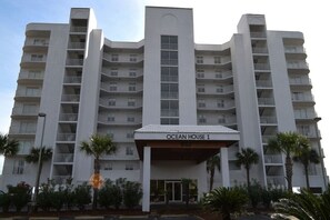 Un hôtel à plusieurs étages doté de balcons, d’une entrée principale et de palmiers au premier plan.