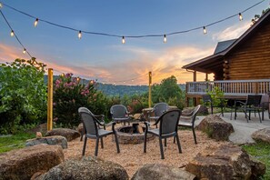 An outdoor seating area with chairs and a fire pit, surrounded by rocks and plants, under string lights.