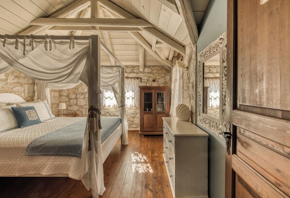 A bedroom with a four-poster bed, stone walls, and a wooden dresser.