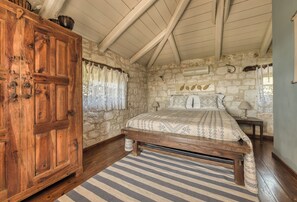 Un dormitorio con pared de piedra, cama de madera, alfombra a rayas y armario de madera.