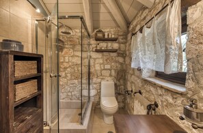 Ein Badezimmer mit Steinwand, Duschkabine aus Glas, Toilette und Waschtisch aus Holz.