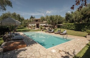 Un área de piscina con sillones de descanso, una pérgola y una terraza de piedra.