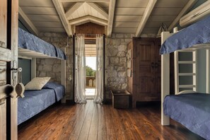 Ein Zimmer mit Steinwand, Holzboden und Etagenbetten mit blauer Bettwäsche.