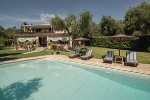 Un área junto a la piscina con sillones de descanso y una zona de estar cubierta.