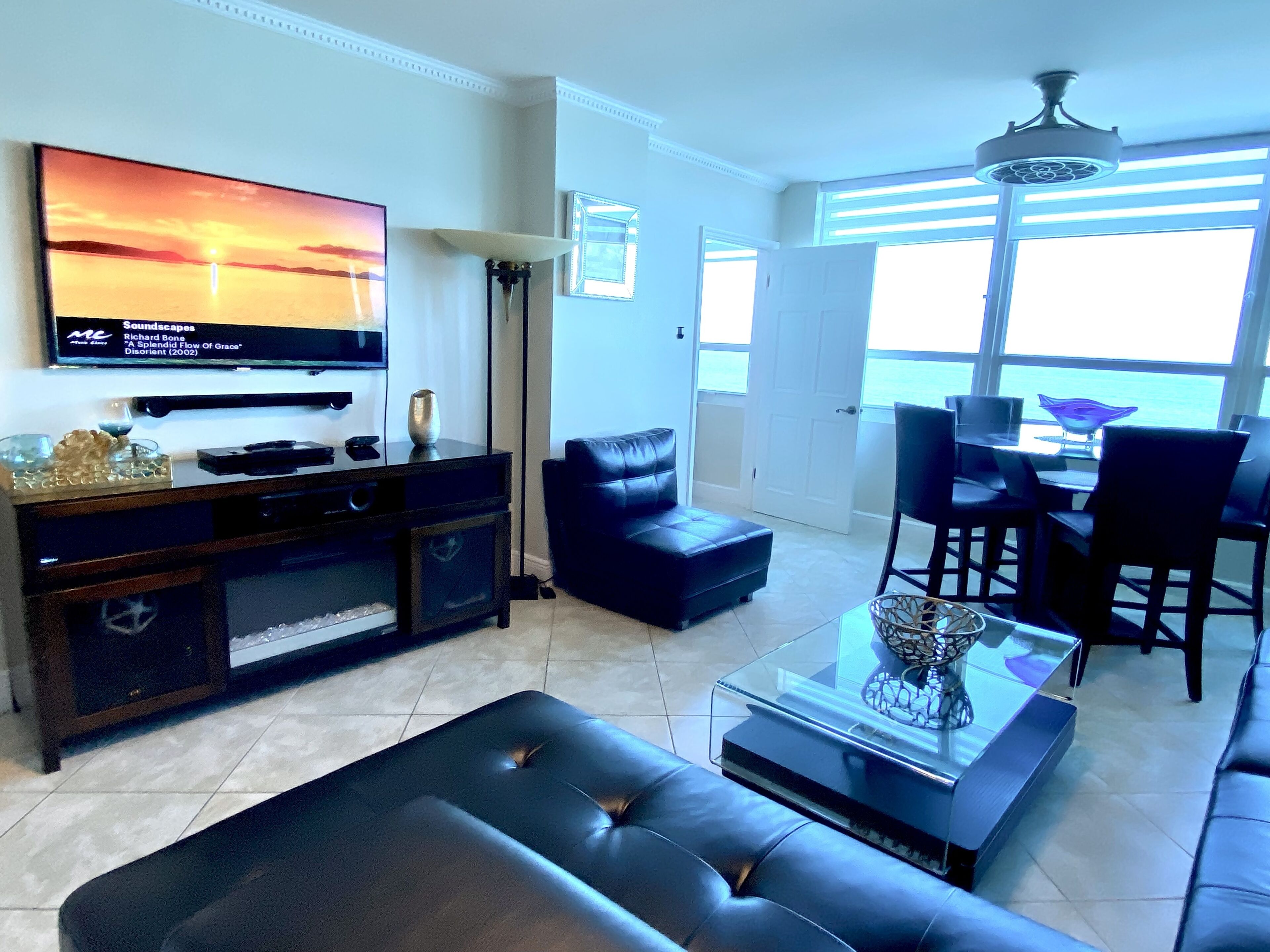 A modern living room with a flat-screen TV, leather sofa, and a dining area with chairs and a table.