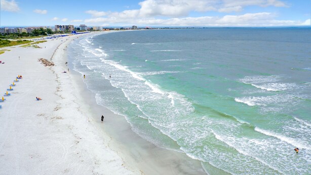 Ein Strand mit weißem Sand, klarem türkisblauem Wasser und einigen Sonnenschirmen.