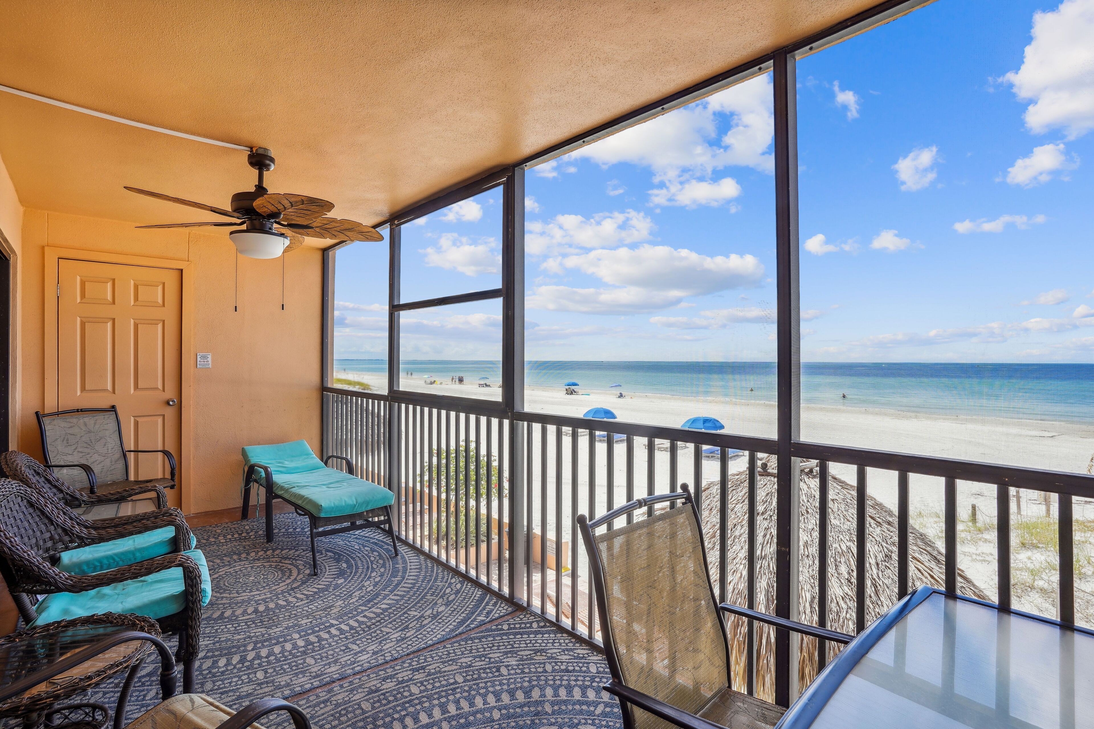 A balcony with wicker furniture, a ceiling fan, and a view of the beach.