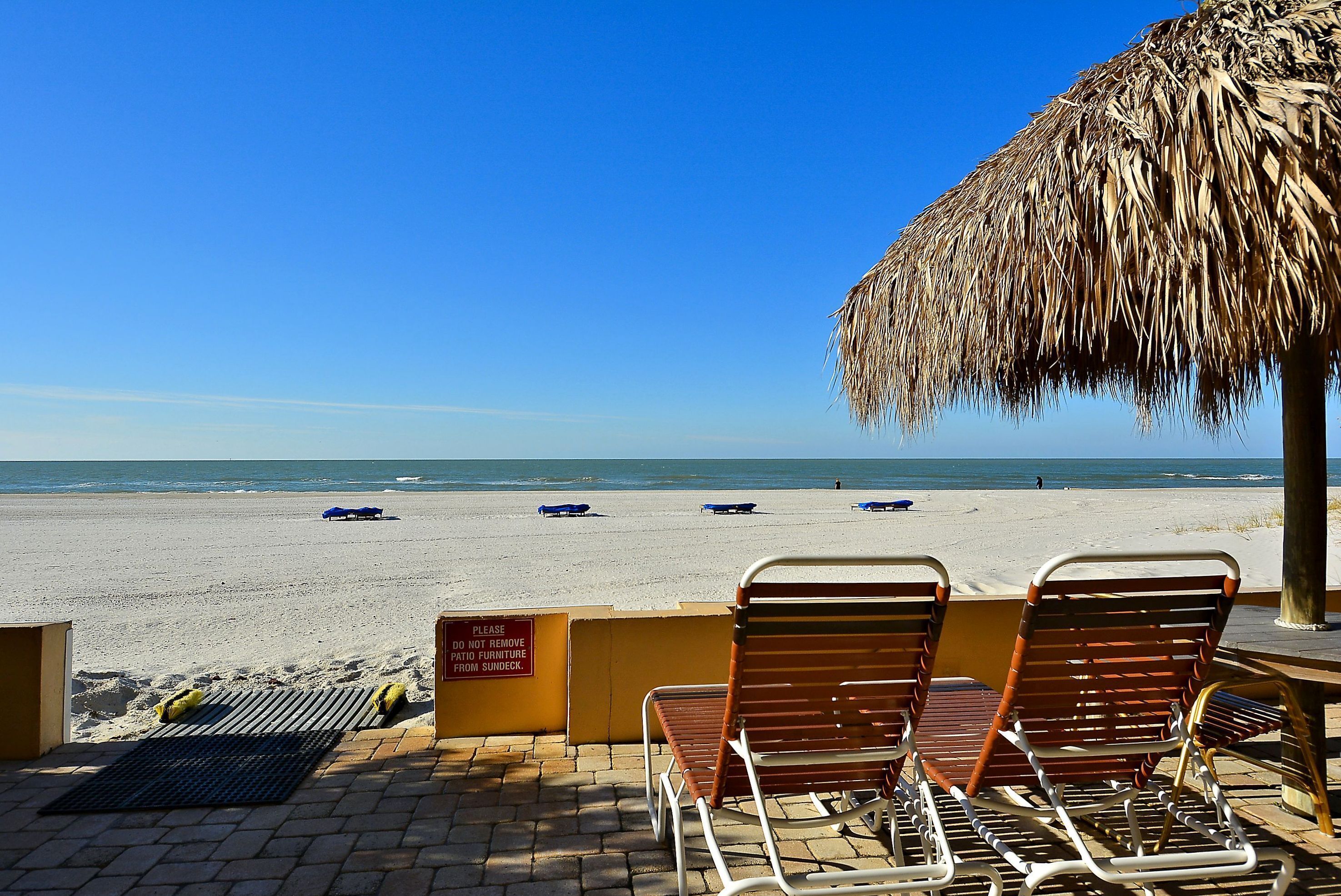 Un espace aménagé près de la plage, avec des chaises longues et un parasol en feuilles de palmier, offrant une vue sur la plage.