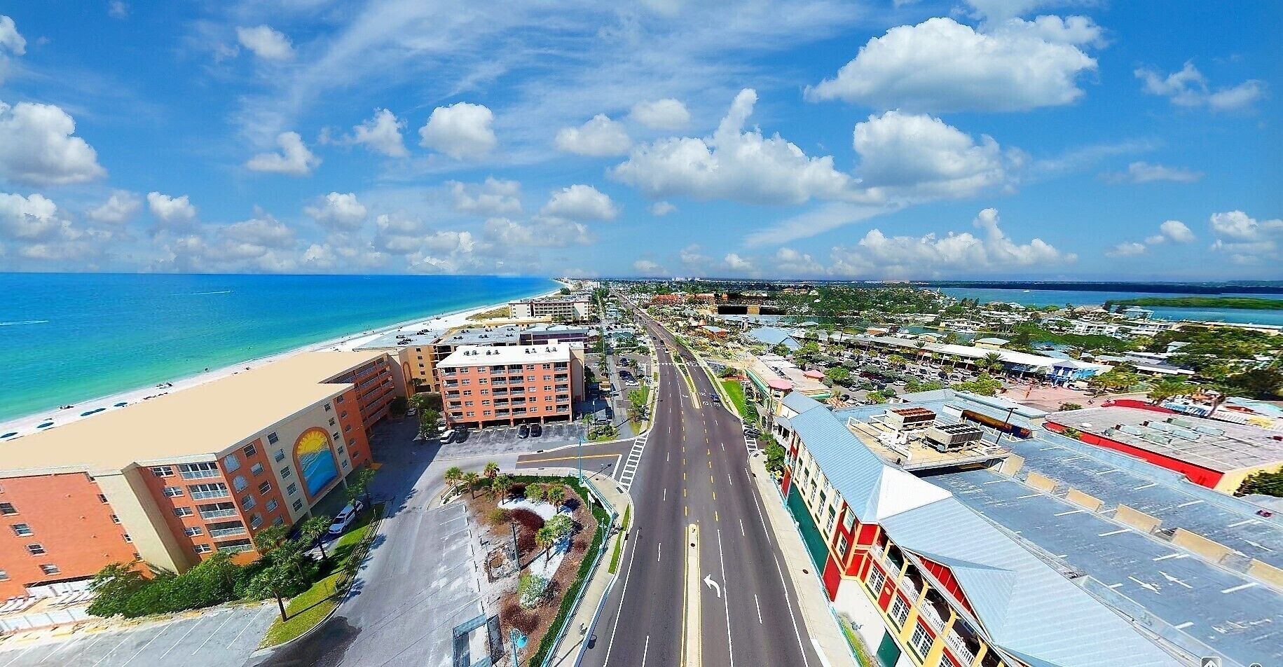 A coastal cityscape with a wide road, beachfront buildings, and a clear blue sky.