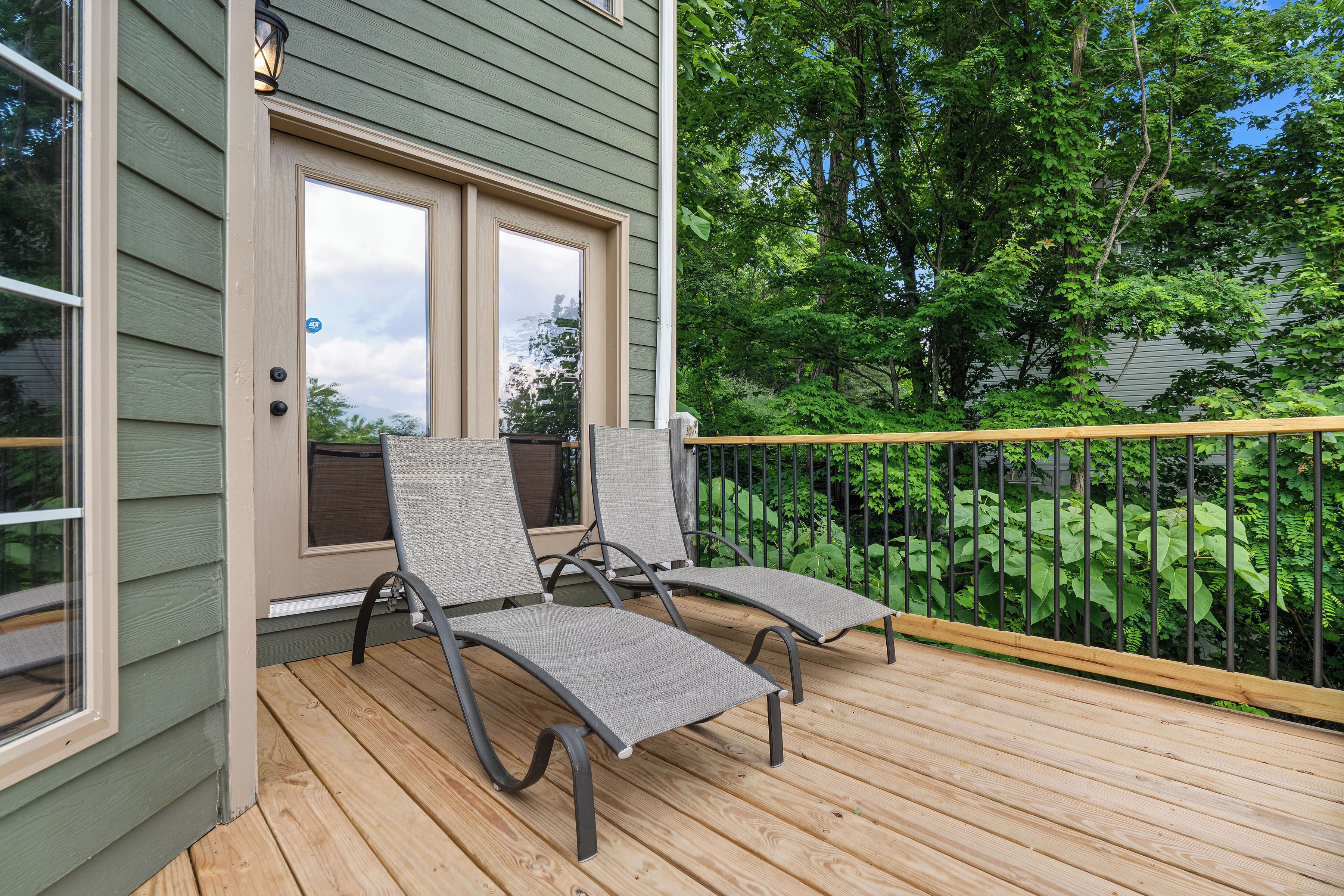 Une terrasse en bois avec deux chaises longues et une porte vitrée donnant sur une pièce.