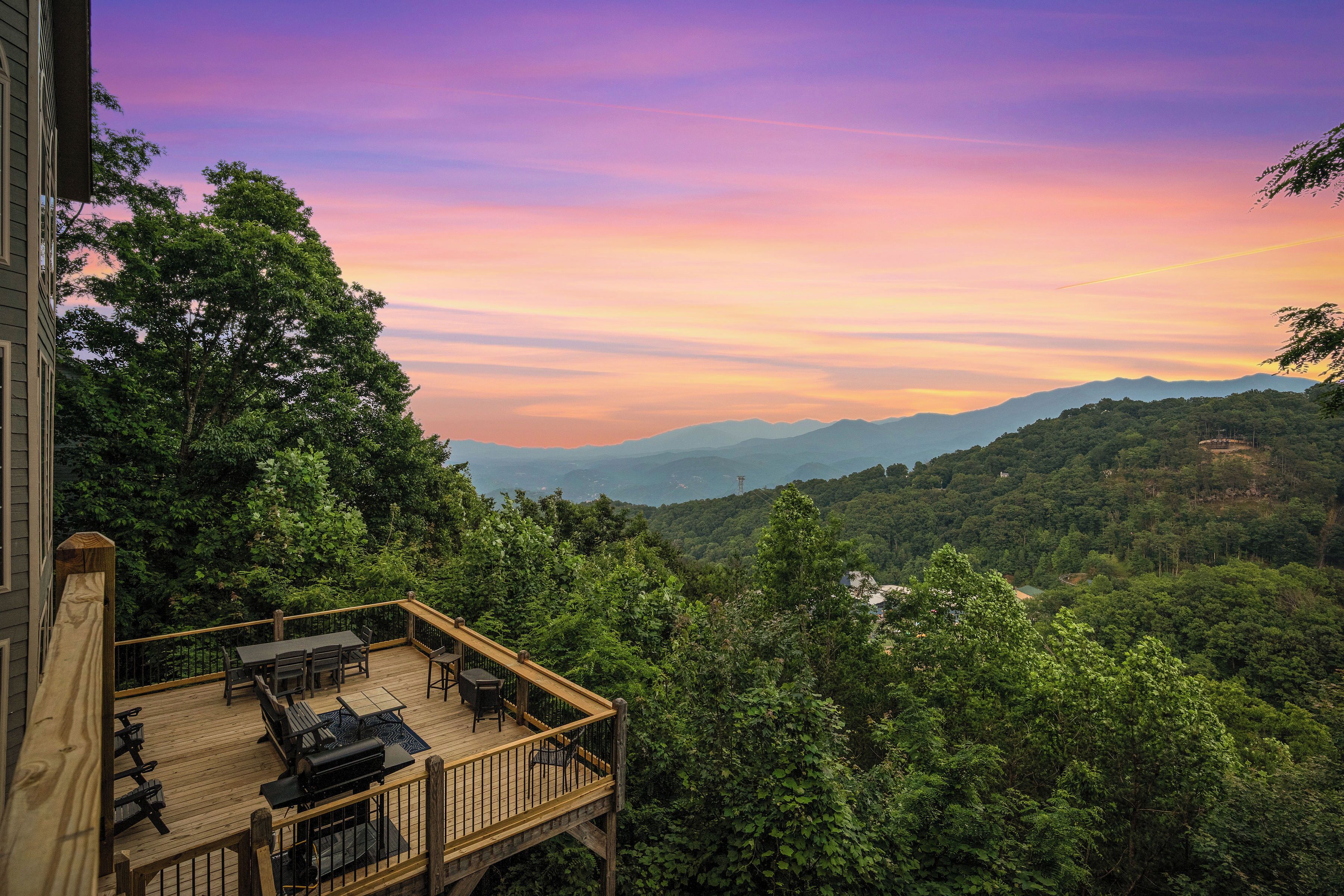 Une terrasse en bois, agréée de mobilier d’extérieur, qui offre une vue sur une forêt luxuriante et des montagnes lointaines.