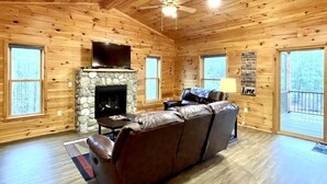 A log cabin interior with a stone fireplace, leather sofa, and a television. - Charming, pet friendly cabin, perfect for fishing, family, hiking and R&R! 2 Bedroom Cabin by RedAwning (Tellico Plains)