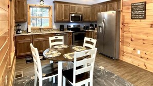 A cabin-style kitchen with wooden walls and ceiling, a dining table with chairs, a refrigerator, and a microwave. - Charming, pet friendly cabin, perfect for fishing, family, hiking and R&R! 2 Bedroom Cabin by RedAwning (Tellico Plains)