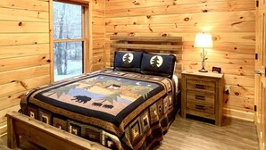 A wooden cabin bedroom with a bed, a nightstand, a lamp, a ceiling fan, and a window. - Charming, pet friendly cabin, perfect for fishing, family, hiking and R&R! 2 Bedroom Cabin by RedAwning (Tellico Plains)