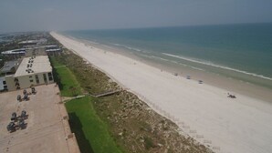 An aerial view of a beach with a long stretch of sand, a few umbrellas, and a building with a flat roof on the left. - Sand Dollar 101 3 Bedroom Condo by RedAwning (St. Augustine)