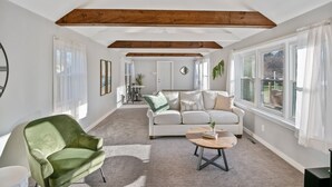 A spacious living room with a white sofa, a green armchair, and a coffee table. There are large windows with white curtains and a wooden ceiling beam. - "sweet Serenity" Stay 10 Minutes From Hershey 3 Bedroom Home by RedAwning (Palmyra)