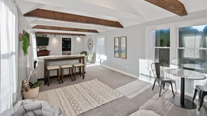 A spacious living area with a high ceiling, exposed wooden beams, a dining table with chairs, a kitchen area, and large windows offering a view. - "sweet Serenity" Stay 10 Minutes From Hershey 3 Bedroom Home by RedAwning (Palmyra)