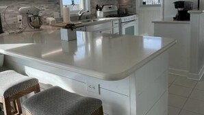 Una cocina moderna con armarios blancos, una isla grande con taburetes y vistas al exterior a través de las ventanas.