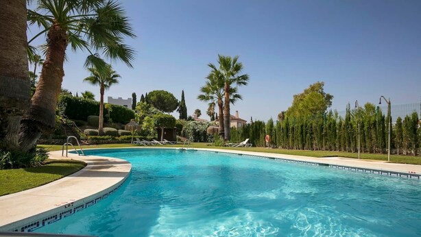 A swimming pool with clear blue water, surrounded by palm trees and a well-maintained lawn. - RDR230 - Apt. Aloha Royal (Marbella)