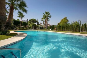 A swimming pool with clear blue water, surrounded by palm trees and a well-maintained lawn. - RDR230 - Apt. Aloha Royal (Marbella)