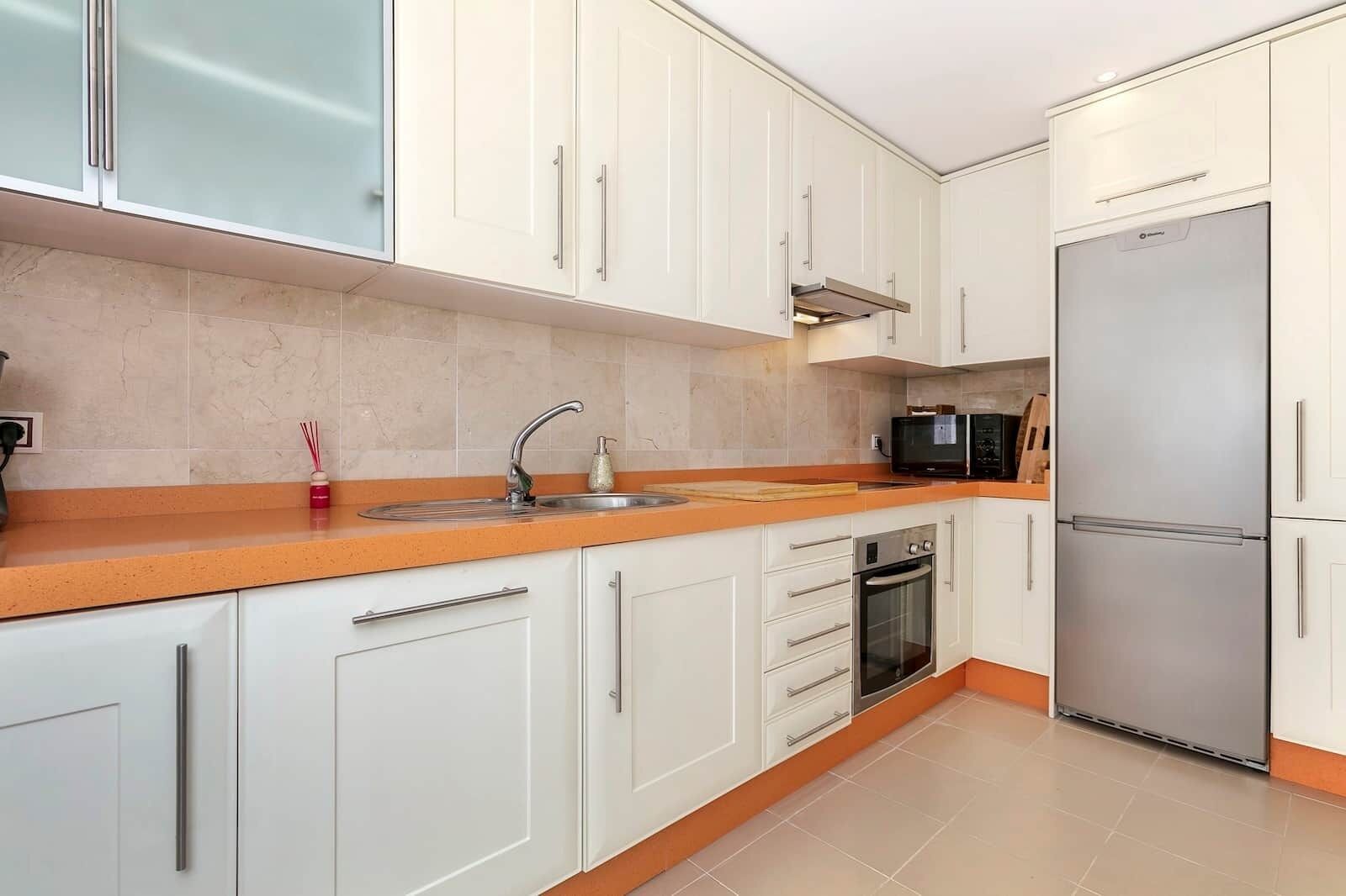 Una cocina moderna con armarios blancos, un refrigerador de acero inoxidable, un microondas y un horno.